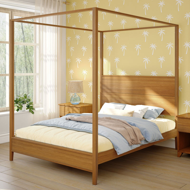 Sunlit modern wooden four-poster canopy bed in a cozy bedroom with yellow palm-print wallpaper, light blue bedding, wooden nightstands with a lamp, and a potted plant