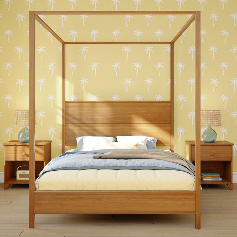 Modern wooden four-poster bed with blue-and-yellow bedding against yellow palm-print wallpaper and bedside lamps