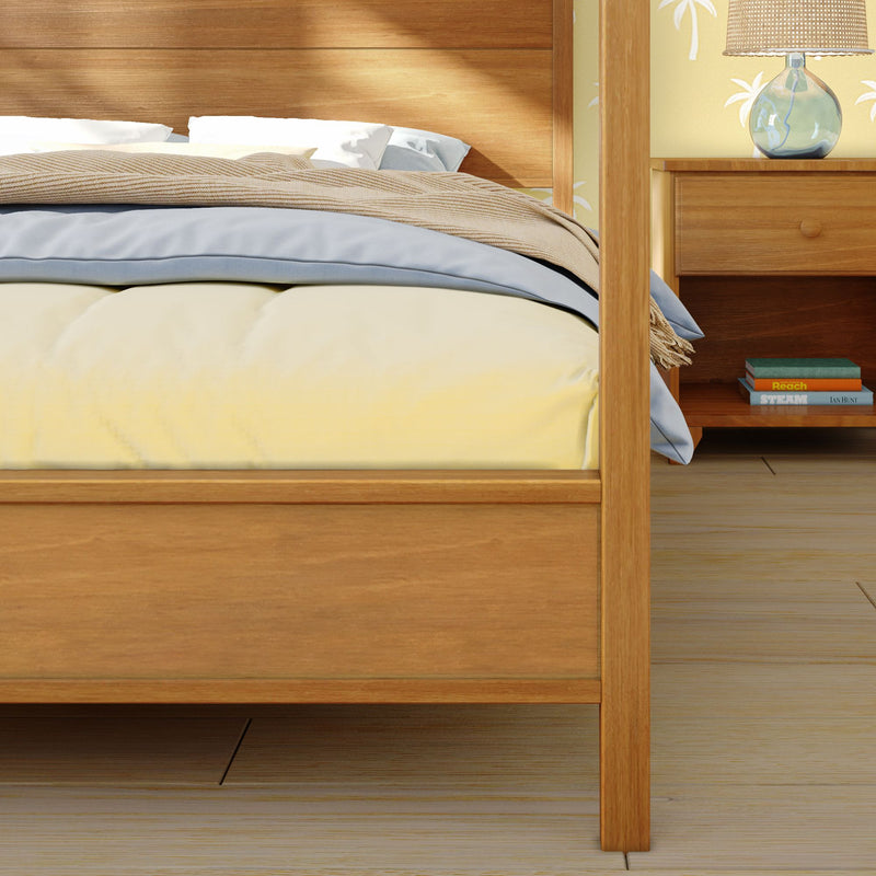 Wooden four-poster bed with yellow comforter, light blue sheets and beige throw beside a matching wood nightstand with lamp and books in a cozy minimalist bedroom interior