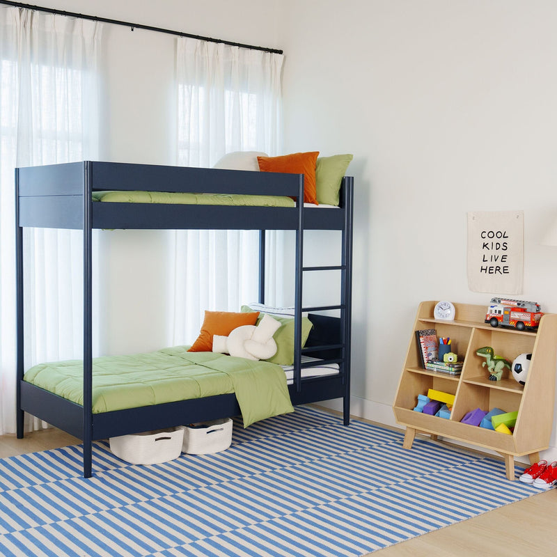 Modern navy metal bunk bed with green bedding and orange pillows in a bright kids' bedroom featuring a toy shelf, soccer ball and blue striped rug under sheer white curtains