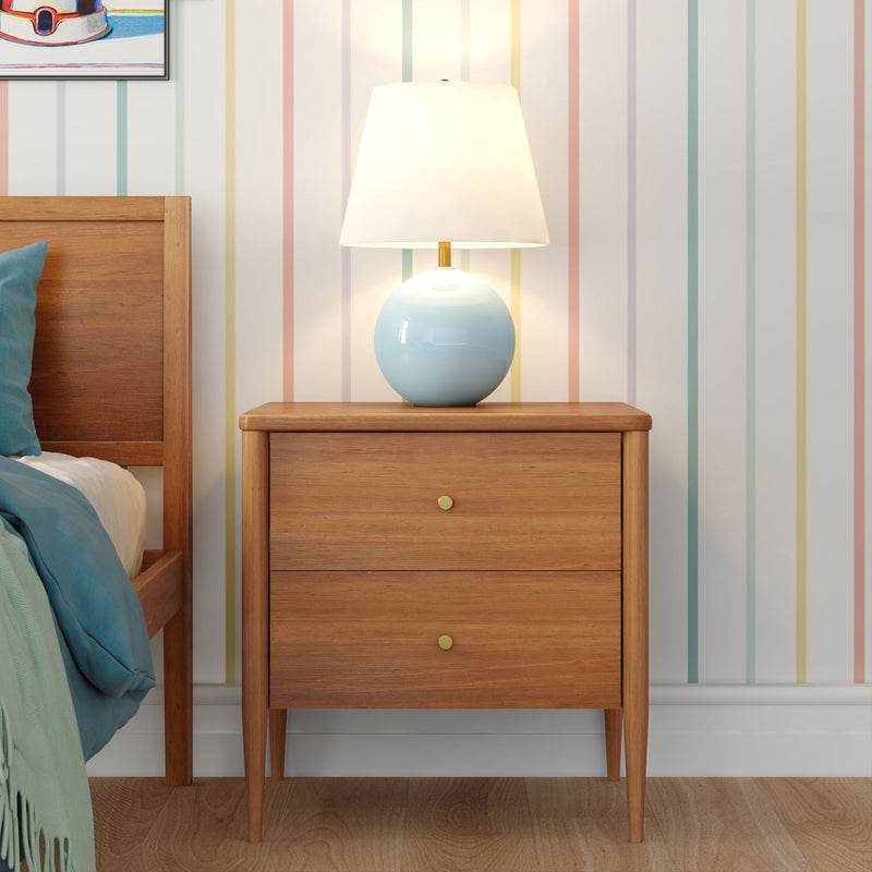 Mid-century modern wooden bedside table nightstand with two drawers and blue ceramic lamp with white shade on hardwood floor, pastel vertical striped wallpaper and teal bedding bedroom decor
