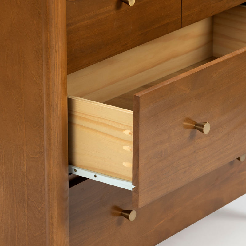 Close-up of a solid wood dresser drawer with visible dovetail joinery, light pine interior, brass knob, metal drawer slide and warm wood grain finish