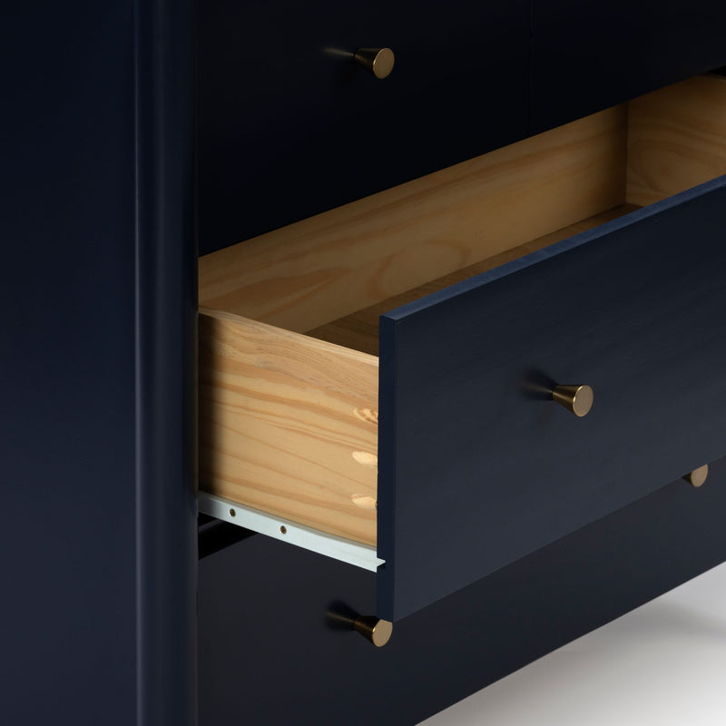 Close-up of a modern navy blue dresser with partially open natural wood drawers and brass knobs, contemporary bedroom storage furniture