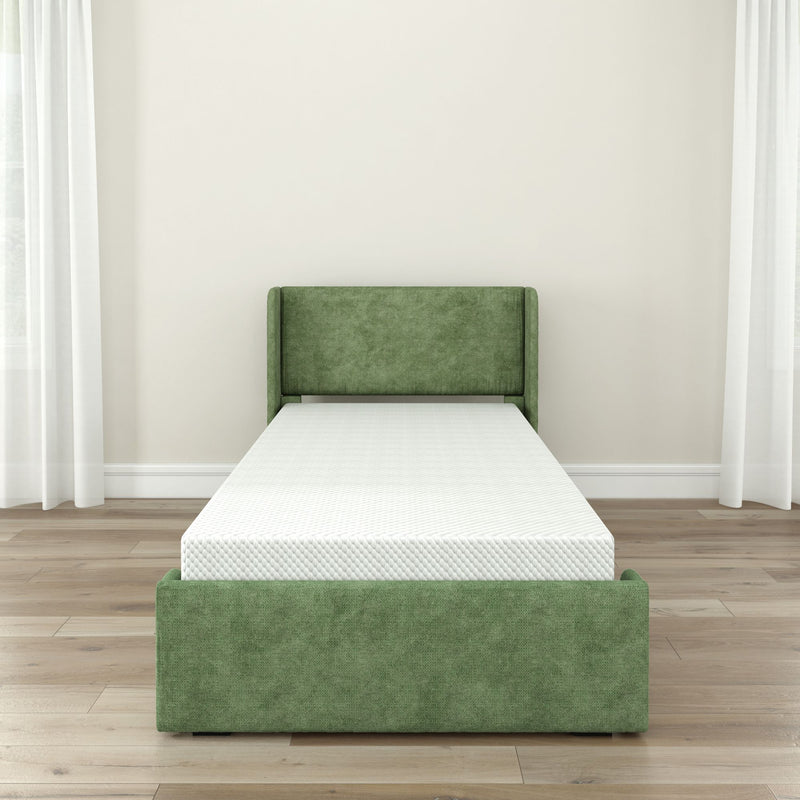 Green upholstered twin bed with white mattress in a modern minimalist bedroom featuring hardwood floors, neutral walls, and sheer white curtains