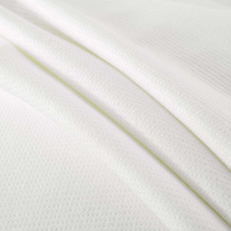 Close-up of white breathable waffle-knit fabric with soft folds and textured surface, cotton-blend bedding or mattress cover material