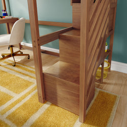 Wooden loft bed with built-in storage stairs beside a yellow geometric rug, white swivel desk chair and teal accent wall in a modern kids' bedroom/home office with hardwood floor