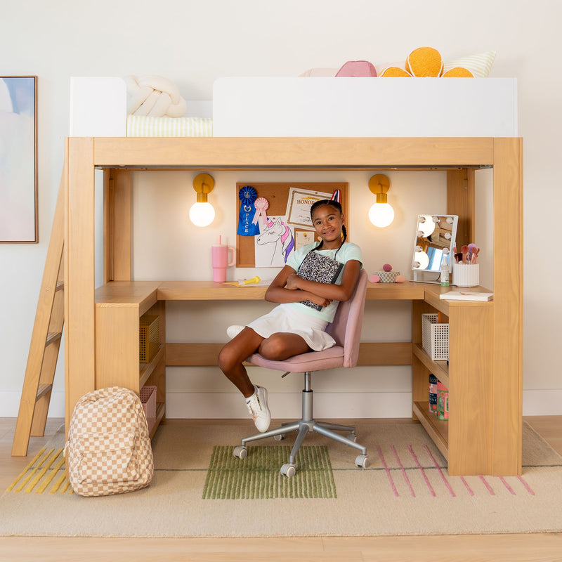 Loft bed with built-in wooden desk and shelves, girl seated in pink chair at organized kids study nook with lamp, mirror and backpack