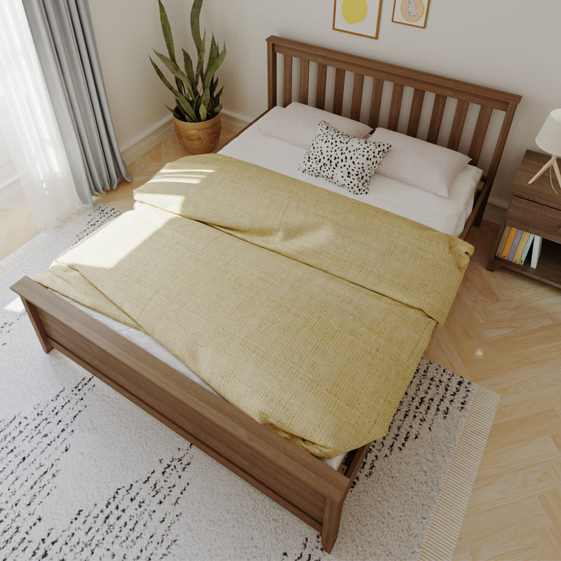 Scandinavian bedroom interior with wooden slat bed frame, yellow duvet, spotted decorative pillow, potted snake plant, bedside lamp and natural light