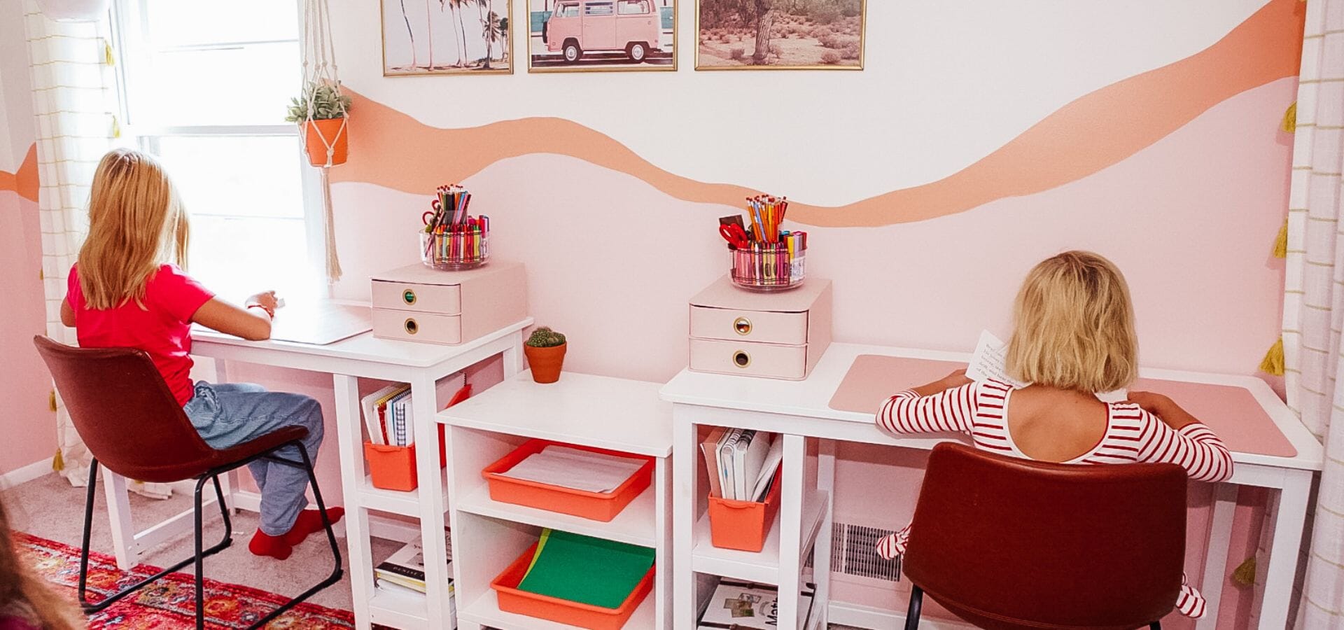 Two sisters sitting at white solid wood desks for kids in pink and orange kids' bedroom