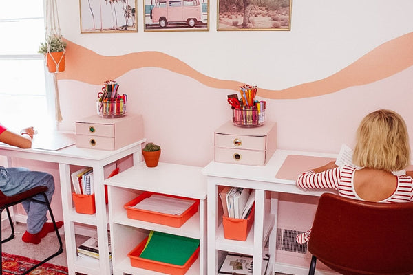 Two sisters sitting at white solid wood desks for kids in pink and orange kids' bedroom