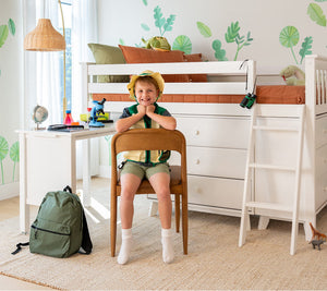 Kids bedroom with white loft bunk bed and study desk, smiling child with green backpack, microscope, orange bedding and jungle wall decals.