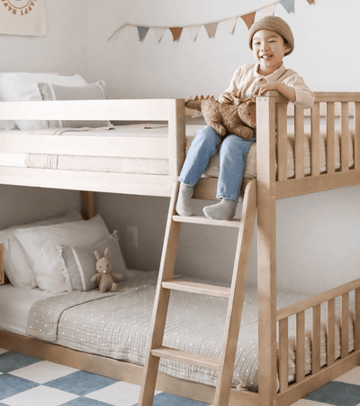 Natural wood twin over twin bunk bed with kid on ladder with playful bedroom decor
