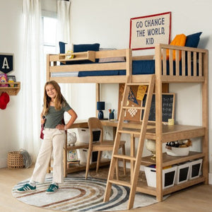 Natural wood kids loft bed with built-in desk, ladder and storage bins in a modern children's bedroom, round rug, wall art reading "Go change the world, kid" and a smiling girl