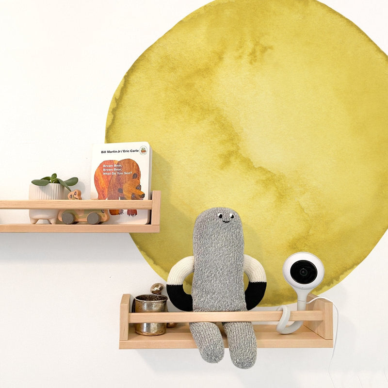 Nursery shelf decor with yellow watercolor circle wall decal wooden shelves knitted gray doll Brown Bear board book small plant and baby monitor