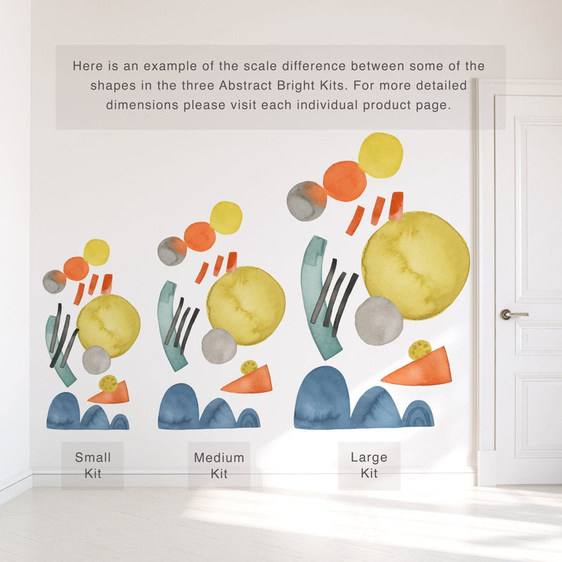 Abstract watercolor wall decals in yellow, orange, teal and blue on a white wall beside a door, showing scale comparison of small, medium and large kits for nursery, kids room and playroom decor