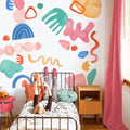 Kids bedroom wall decals with colorful abstract mural, cozy single bed with stuffed animal, pink curtains and wooden nightstand, children's room decor