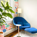 Cozy modern reading nook with blue lounge chair and ottoman, colorful abstract wall mural, floor lamp and large green houseplant by sunlit window