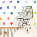 Modern nursery playroom featuring colorful watercolor polka dot wall decals, black wire mid-century chair draped with a gray throw, gray-and-white striped rug, white faux fur rug and wooden toys