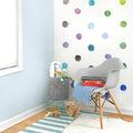 Nursery reading nook with white Eames-style chair, blue-and-white striped rug and blanket, colorful watercolor polka dot wall decals, gray felt toy storage basket, wooden floor and natural light