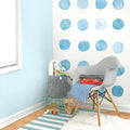 Kids nursery corner with blue watercolor polka dot wall decals, modern gray Eames-style chair, striped teal rug, toy basket and stuffed animals