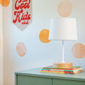 Kids room decor: white table lamp on a mint-green dresser with stacked children's books, orange watercolor circle wall decals and a "The Cool Kids Club" fabric banner