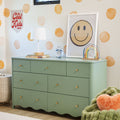 Kids bedroom with sage green dresser, white lamp, blue alarm clock, wooden abacus, smiley face print and orange polka-dot wall
