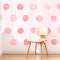 Modern wooden chair on hardwood floor against pastel pink watercolor polka dot wallpaper — nursery accent wall and kids' room decor