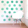 White Eames-style chair on hardwood floor in front of a white accent wall with green watercolor polka dot wall decals, modern nursery or kids' room interior decor