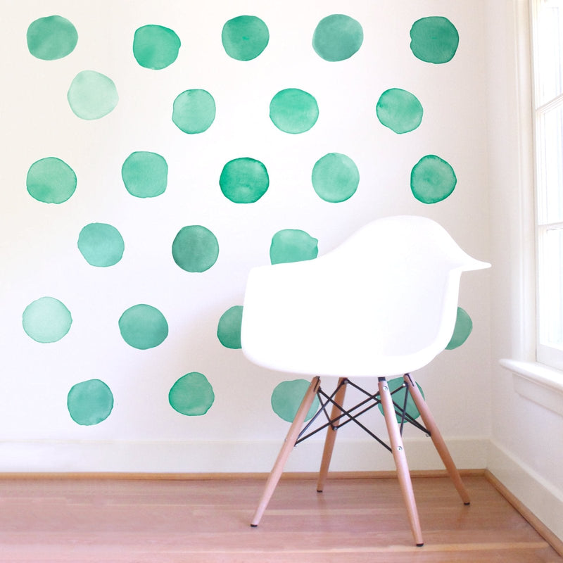 White Eames-style chair on hardwood floor in front of a white accent wall with green watercolor polka dot wall decals, modern nursery or kids' room interior decor