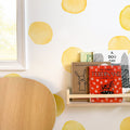 Children's books on a wooden nursery bookshelf with a red "Ferdinand" cover, round yellow polka-dot wall decals, light oak table and window light