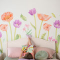 Child reading a book in a pastel kids' bedroom with large watercolor floral wallpaper mural, pink bed and cozy pillows