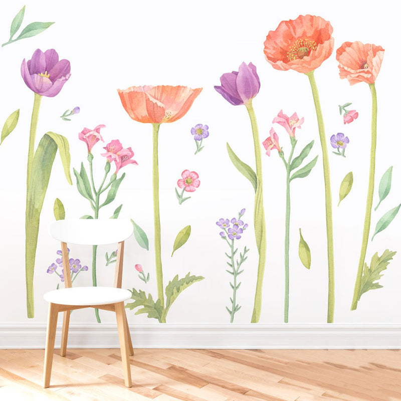 Watercolor floral wall decal mural featuring orange poppies, purple tulips and pastel wildflowers over a white chair on hardwood floor — removable nursery wall art and vinyl sticker décor for bedroom or living room