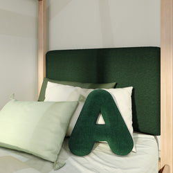 Plush green letter A pillow with mint and white cushions on light wood bed in modern children's bedroom with dark green upholstered headboard