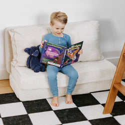 Child reading a bedtime storybook on a couch with a stuffed animal, promoting kids' literacy and imagination.