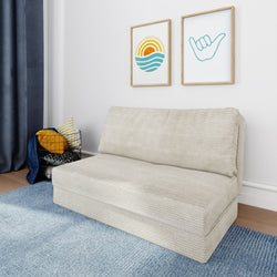 Beige convertible loveseat sofa bed on a blue area rug in a modern coastal-style living room with a wire basket of yellow and patterned throw pillows and framed sun and shaka wall art