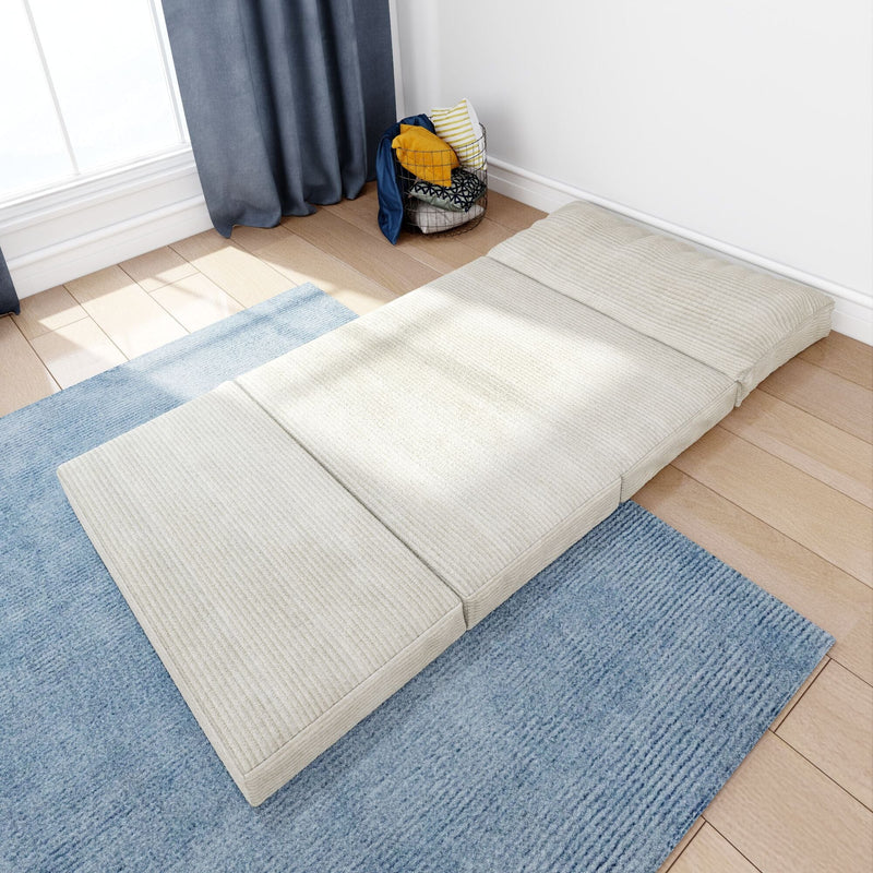 Beige tri-fold foldable floor mattress futon on blue rug in a bright minimalist bedroom corner, space-saving guest bed on hardwood floor with pillow storage basket