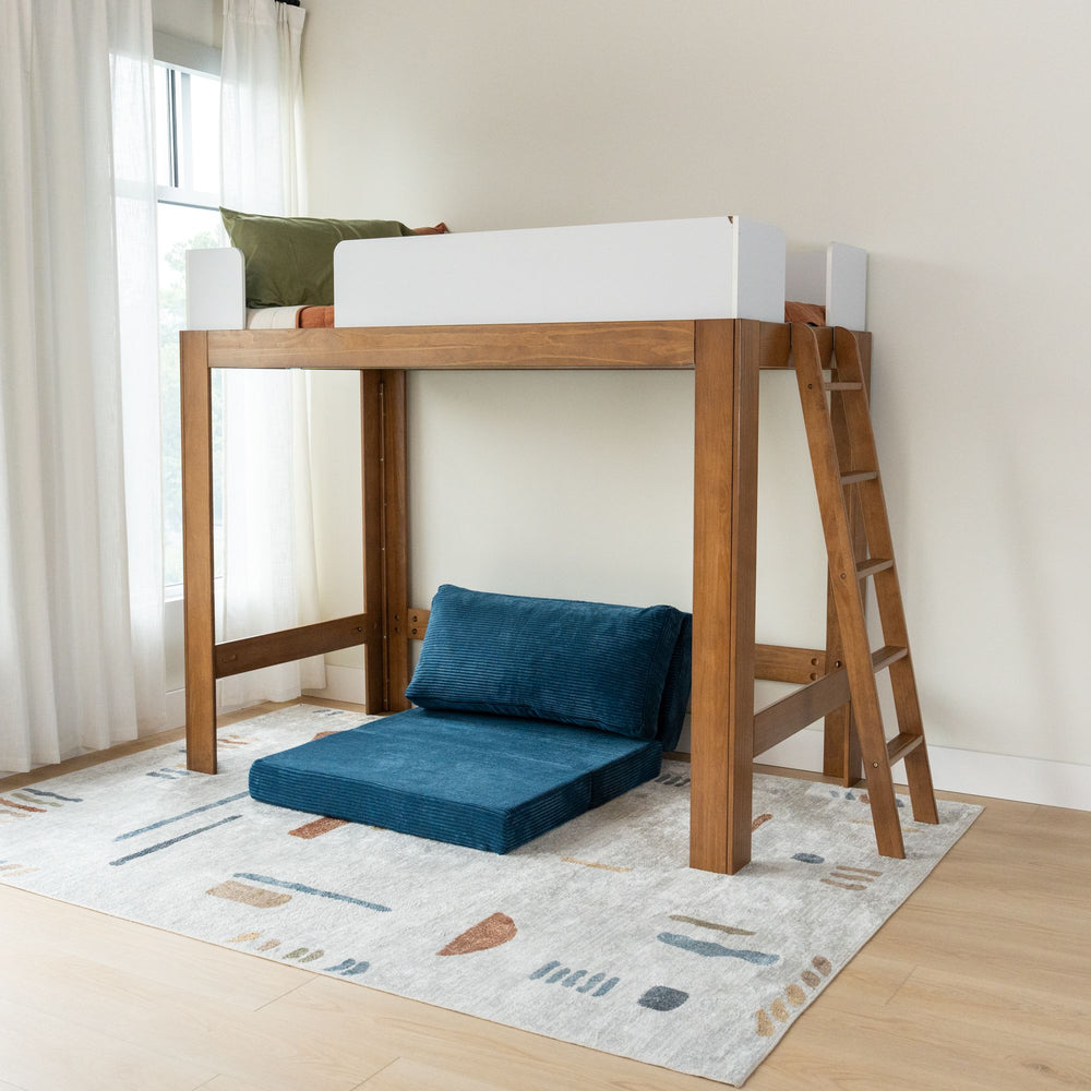 Wooden loft bed with ladder and navy blue lounge seating underneath on a modern geometric rug in a bright bedroom.