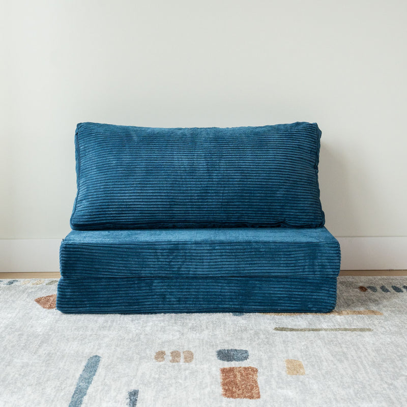 Blue corduroy folding couch on a modern geometric-patterned rug in a minimalist room.