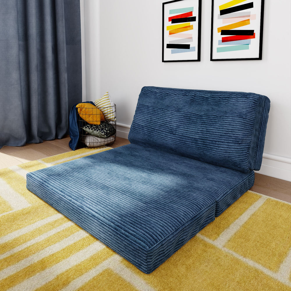 Blue corduroy folding futon couch on yellow geometric rug in modern living room with art on the wall.