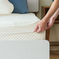 Person adjusting a white fitted sheet on a comfortable memory foam mattress.
