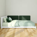 Low-profile white wooden platform bed with dark green upholstered headboard, green-striped bedding and pillows in a minimalist bedroom on light hardwood floor