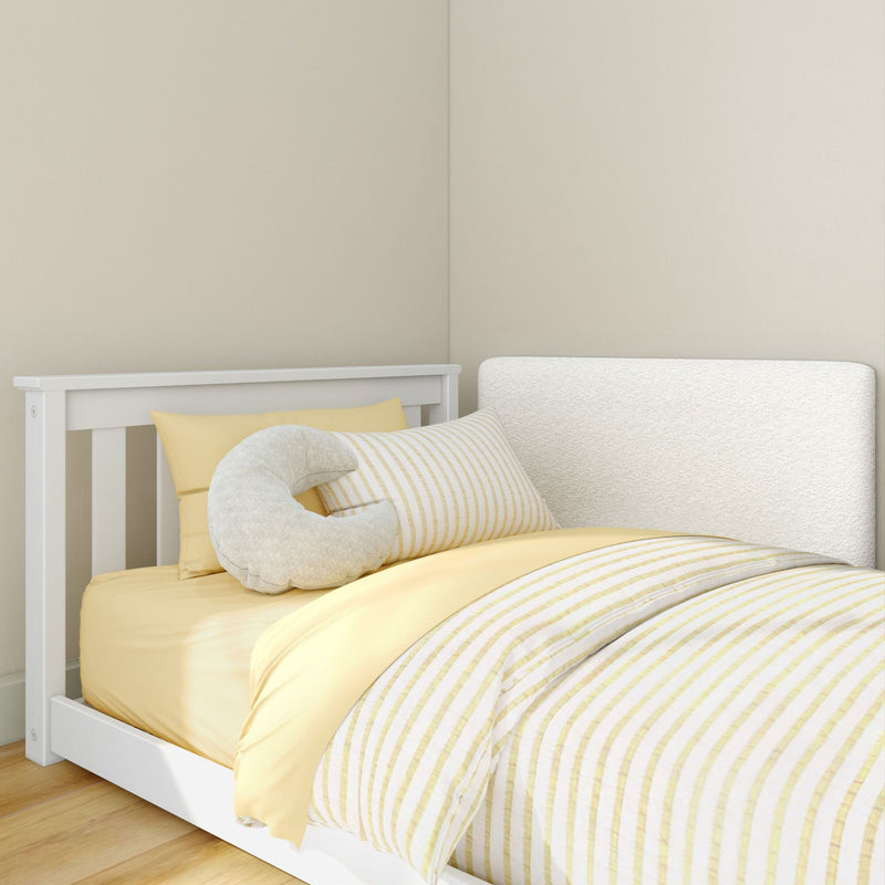 White wooden toddler bed with yellow fitted sheet, striped yellow-and-white duvet, crescent moon plush pillow on hardwood floor — cozy nursery decor