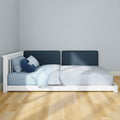 Modern white low platform bed with navy upholstered headboard, light blue striped bedding and hardwood floor in a minimalist bedroom