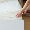 Person adjusting a white mattress protector on a bed for comfort and protection.