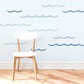 Scandinavian white wooden chair on light hardwood floor against a pale blue wall with blue wave wall decals — coastal nursery decor and modern minimalist interior
