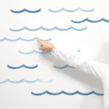 Child's hand pointing at blue wave wall decals on white wall, ocean-themed nursery and kids room decor
