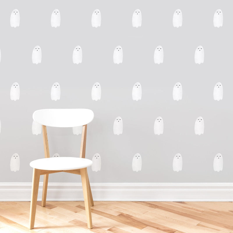White wooden chair on hardwood herringbone floor against a light grey wall covered in repeating cute white ghost wallpaper pattern, modern minimalist nursery decor