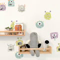 Nursery wall with colorful monster decals, wooden floating shelves holding knit doll, "Brown Bear" book, plant and baby monitor camera