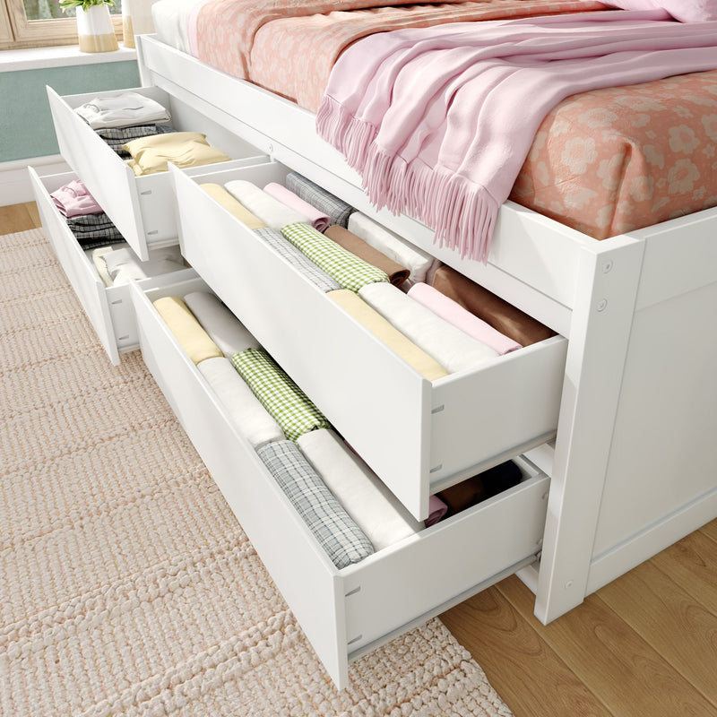 White platform bed with built-in under-bed storage drawers open showing neatly folded pastel bedding and clothes, space-saving bedroom storage solution