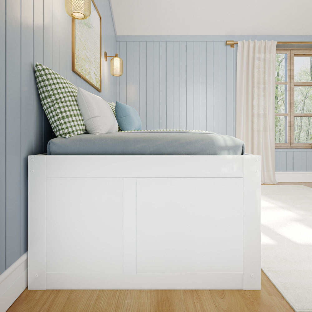 Cozy bedroom interior with a modern white bed, blue and green pillows, blue paneled walls, and natural light from a large window.